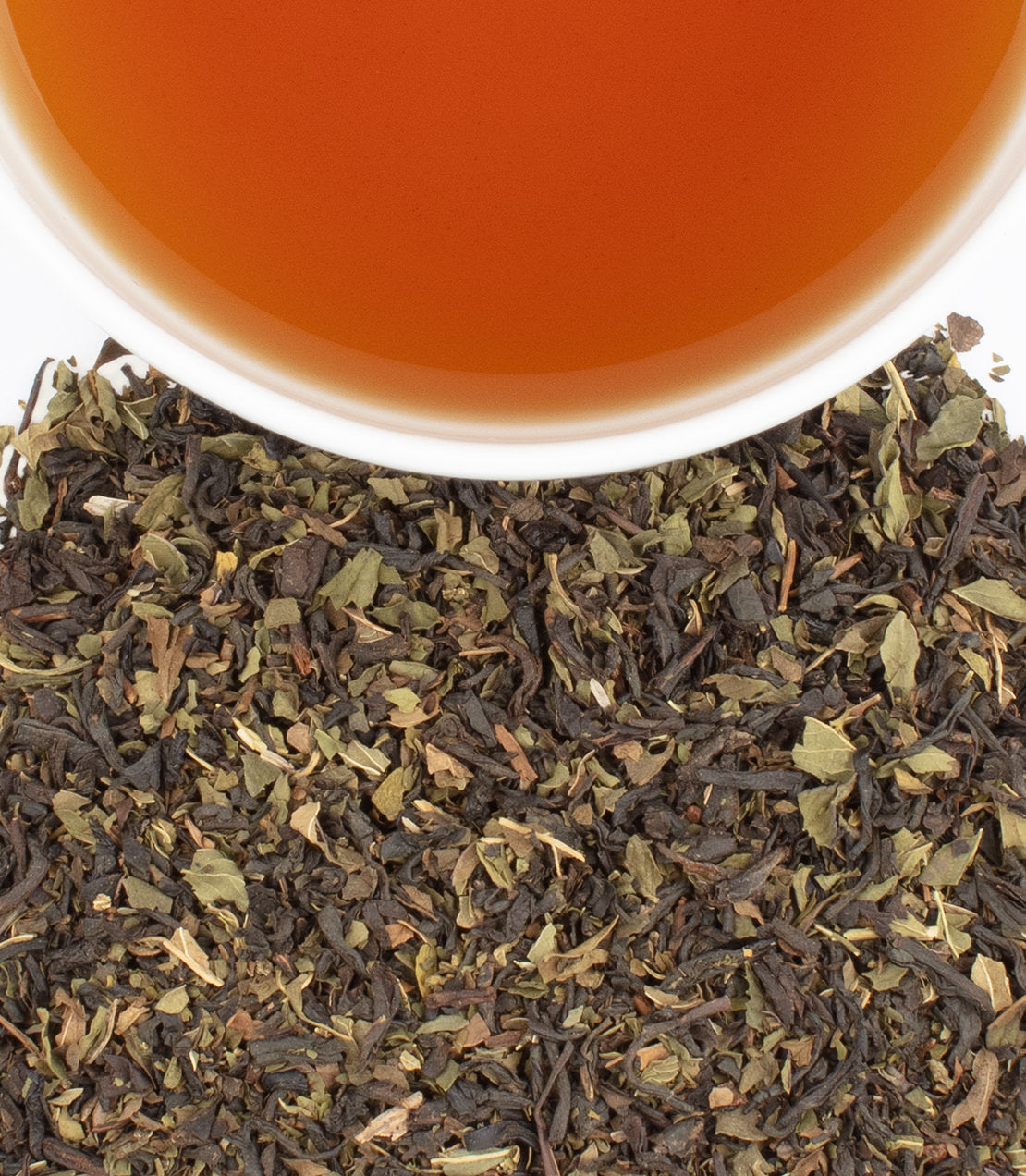 A cup of brewed chocolate mint tea above a pile of loose chocolate mint tea leaves.