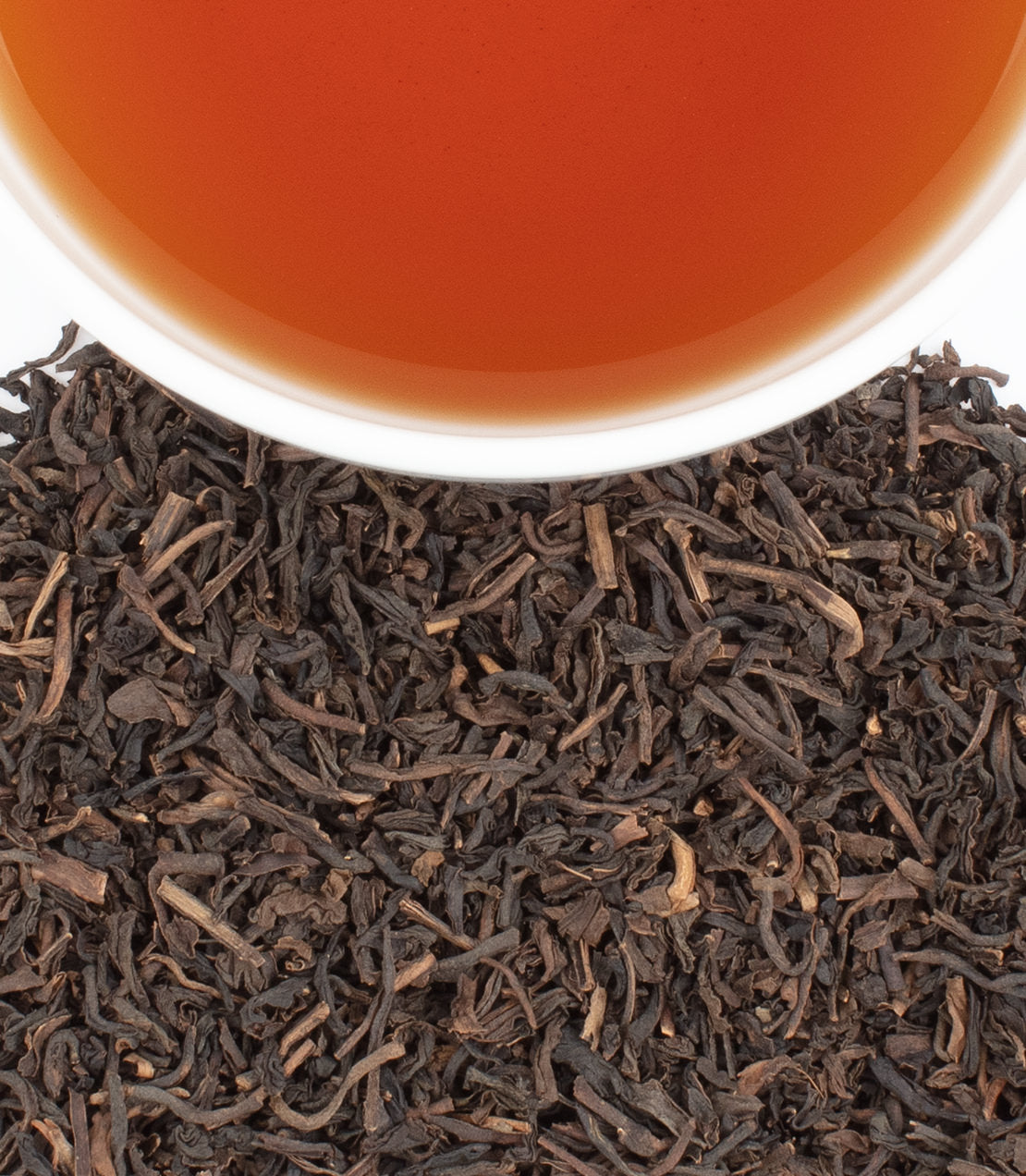 A cup of decaf chocolate tea above a pile of loose black tea leaves, showcasing rich color and texture.