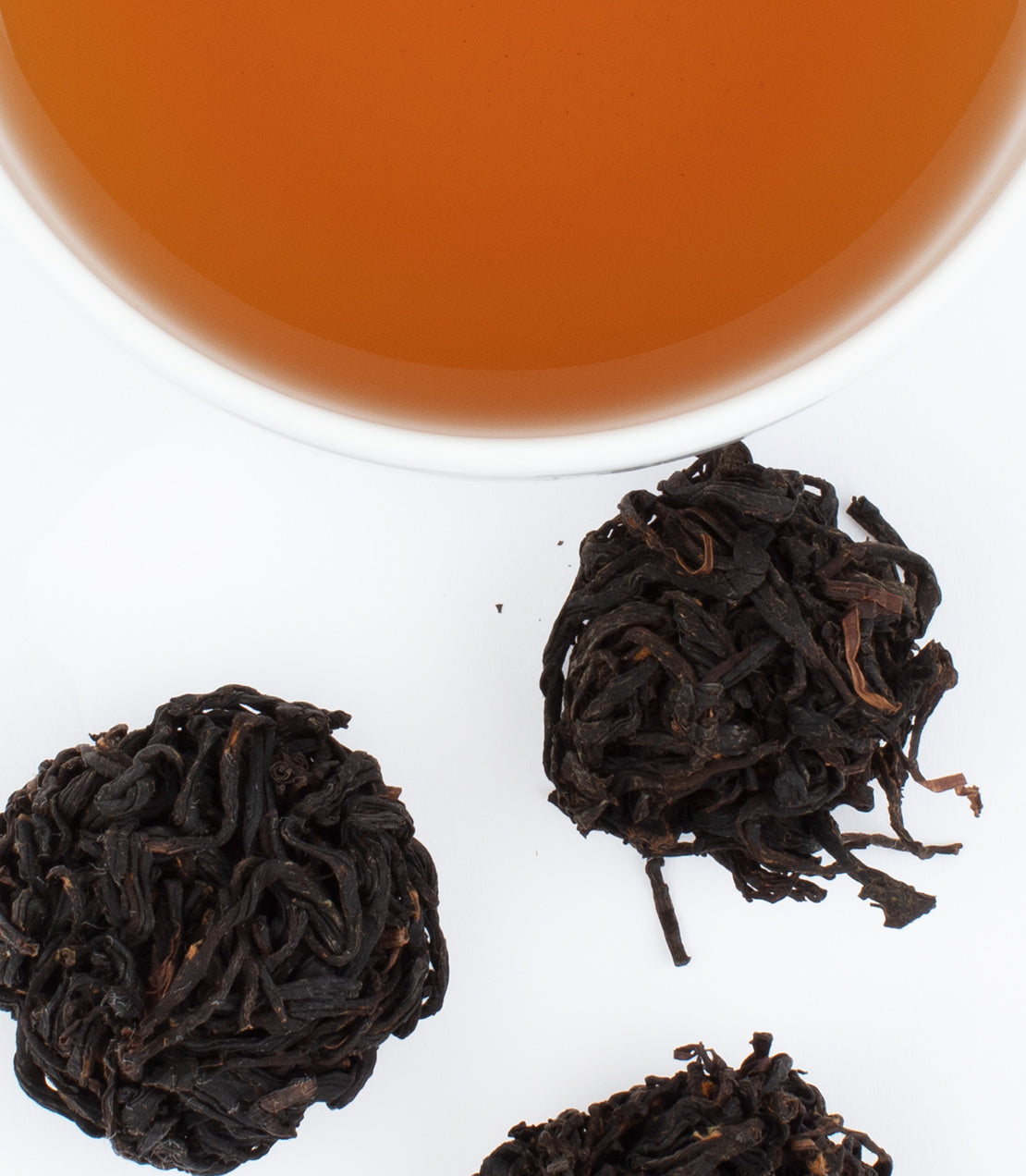 Fujian Black tea leaves in compressed balls beside a cup of brewed amber tea.