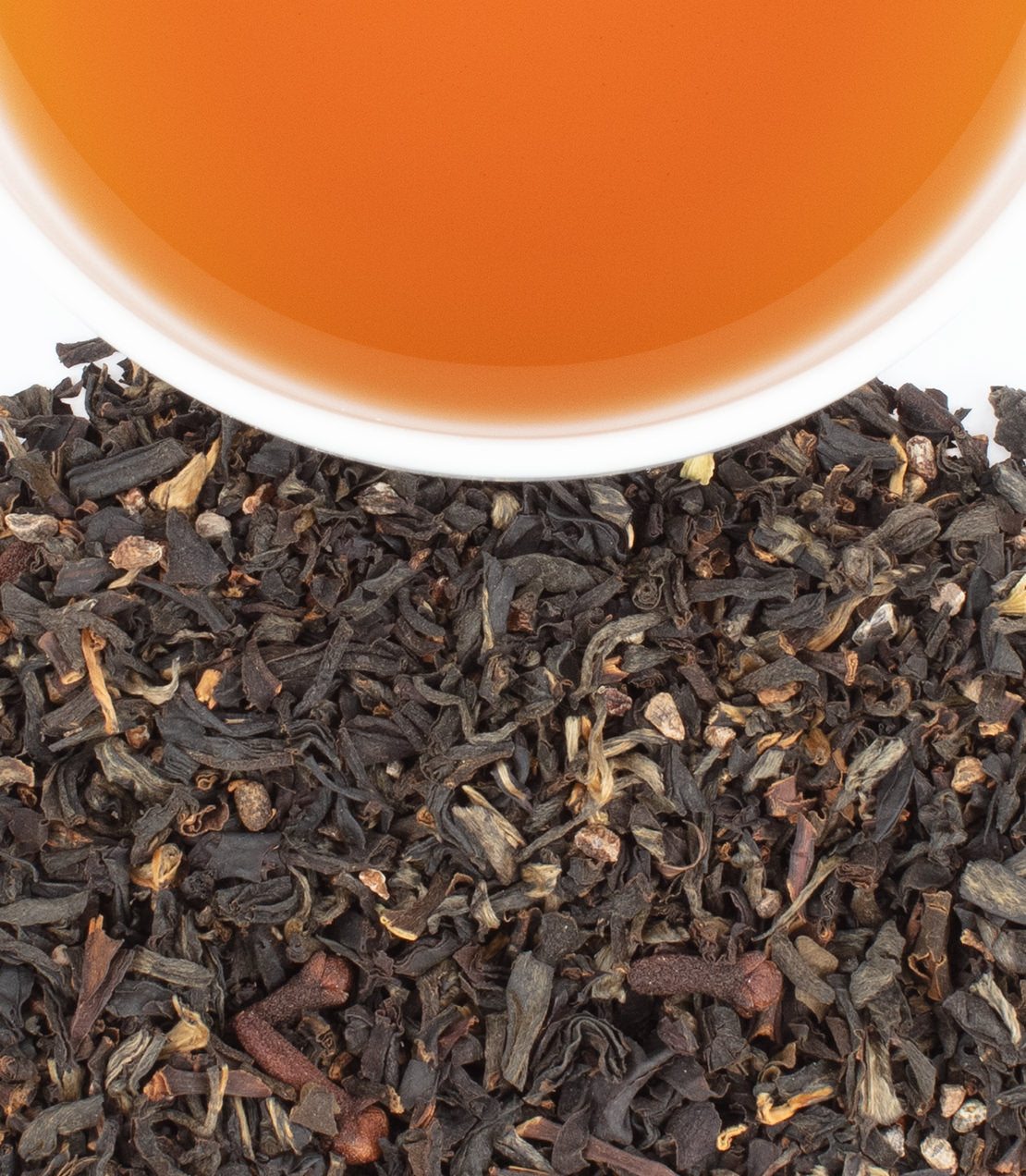 A close-up of loose Wild Spiced Ceylon tea leaves with a cup of brewed tea above, showcasing rich colors and textures.
