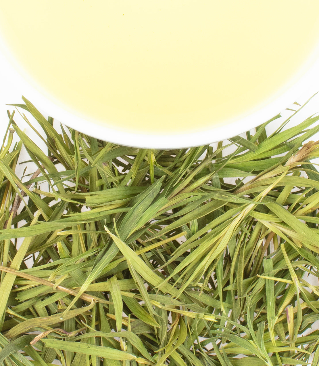 Fresh bamboo leaves arranged beneath a bowl of light green bamboo tea, showcasing natural textures and colors.