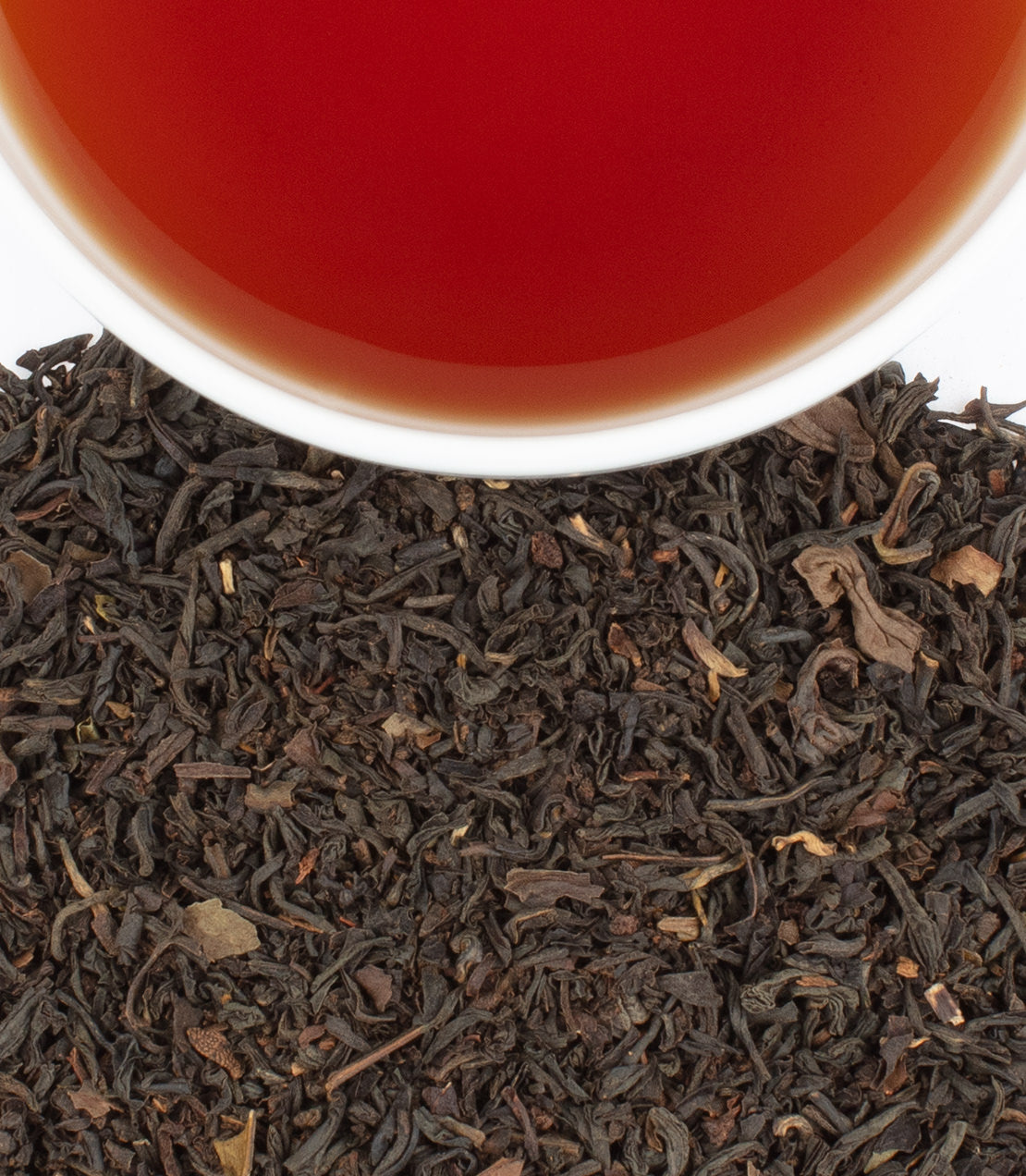A cup of brewed Earl Grey tea above loose black tea leaves, showcasing its rich color and aromatic blend.