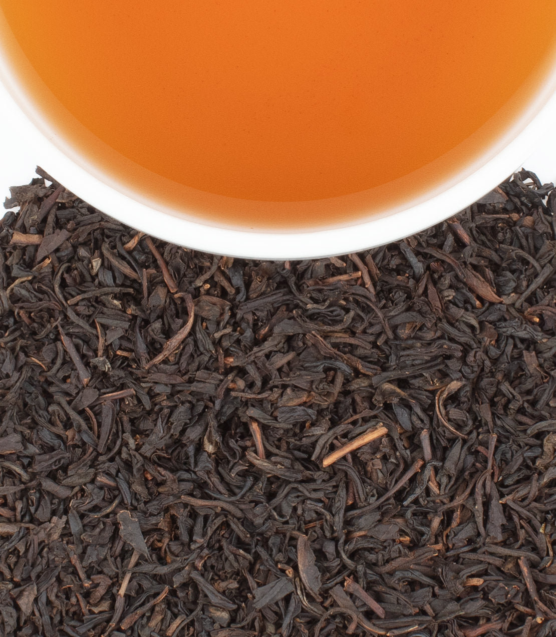 A close-up of loose black tea leaves with a cup of brewed tea above, showcasing rich amber color.