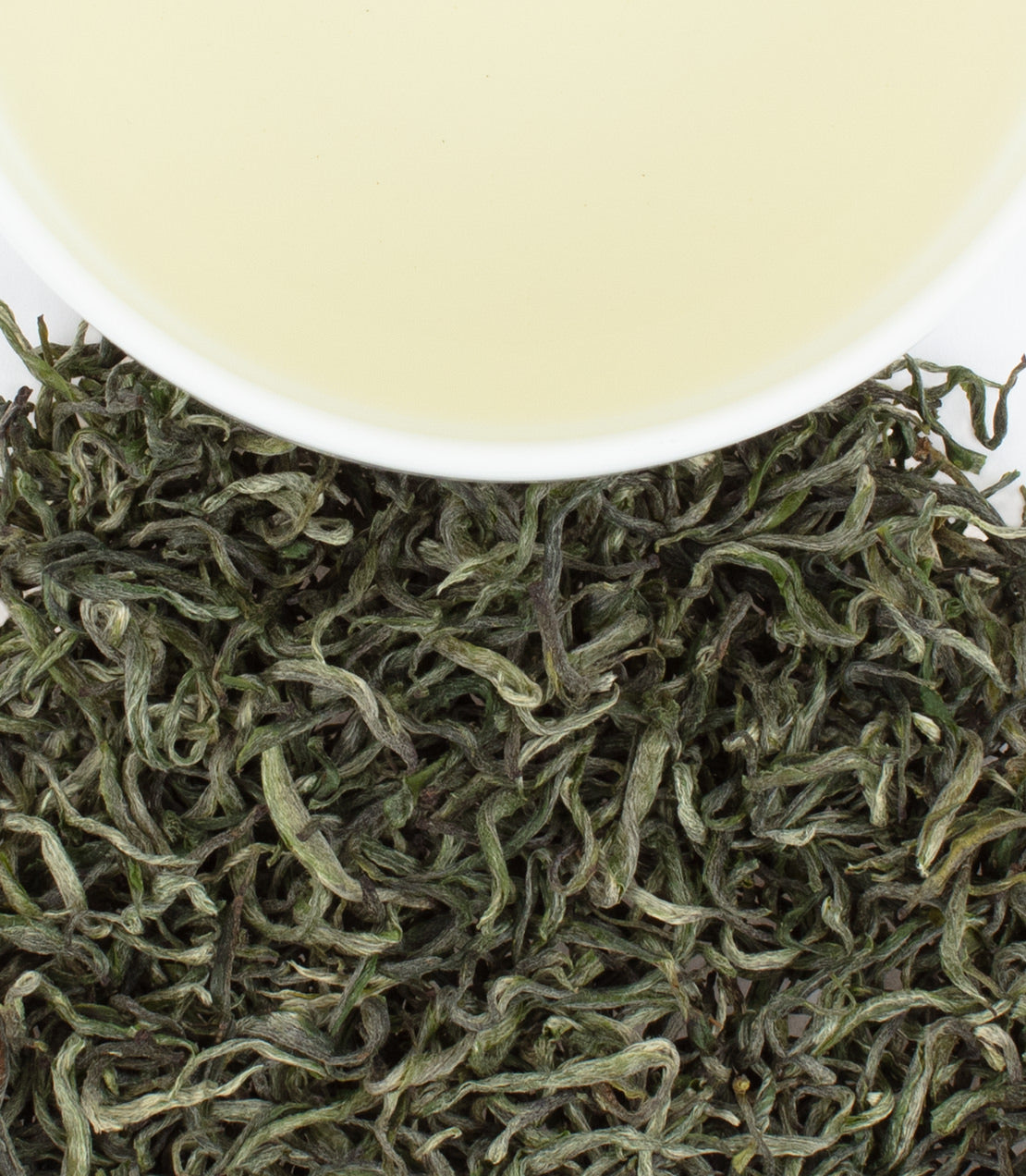 Golden Green tea leaves with a cup of pale green tea above, showcasing the tea's delicate color and texture.