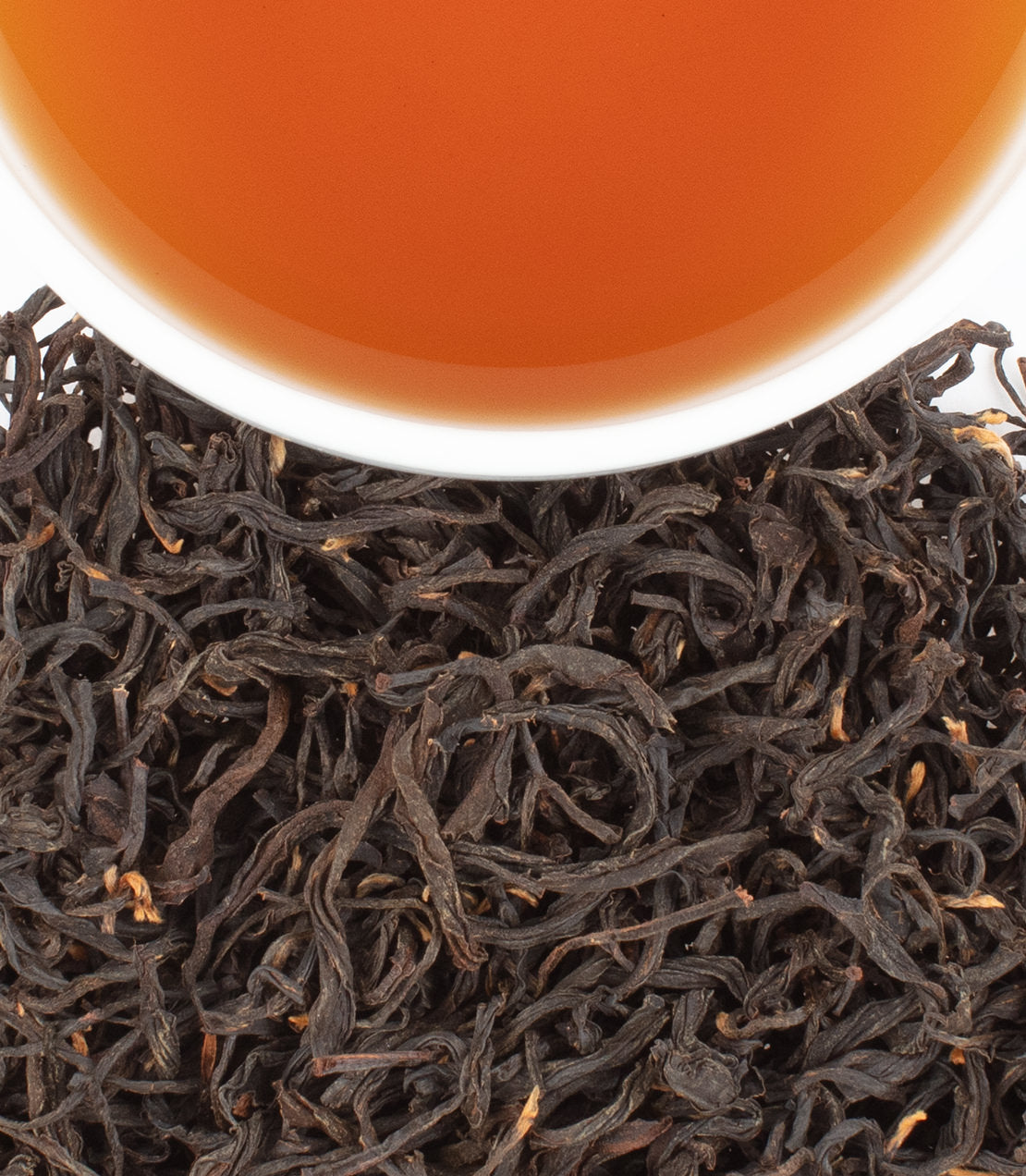 A close-up of Taiwan Honey Black tea leaves with a cup of brewed tea above, showcasing rich colors and textures.