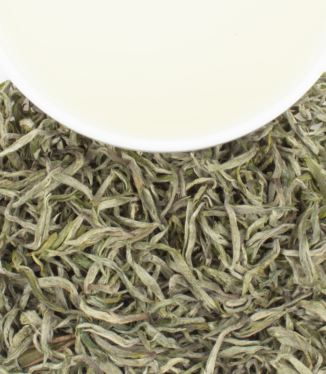A pile of dried green tea leaves with a cup of light-colored brewed tea above them.