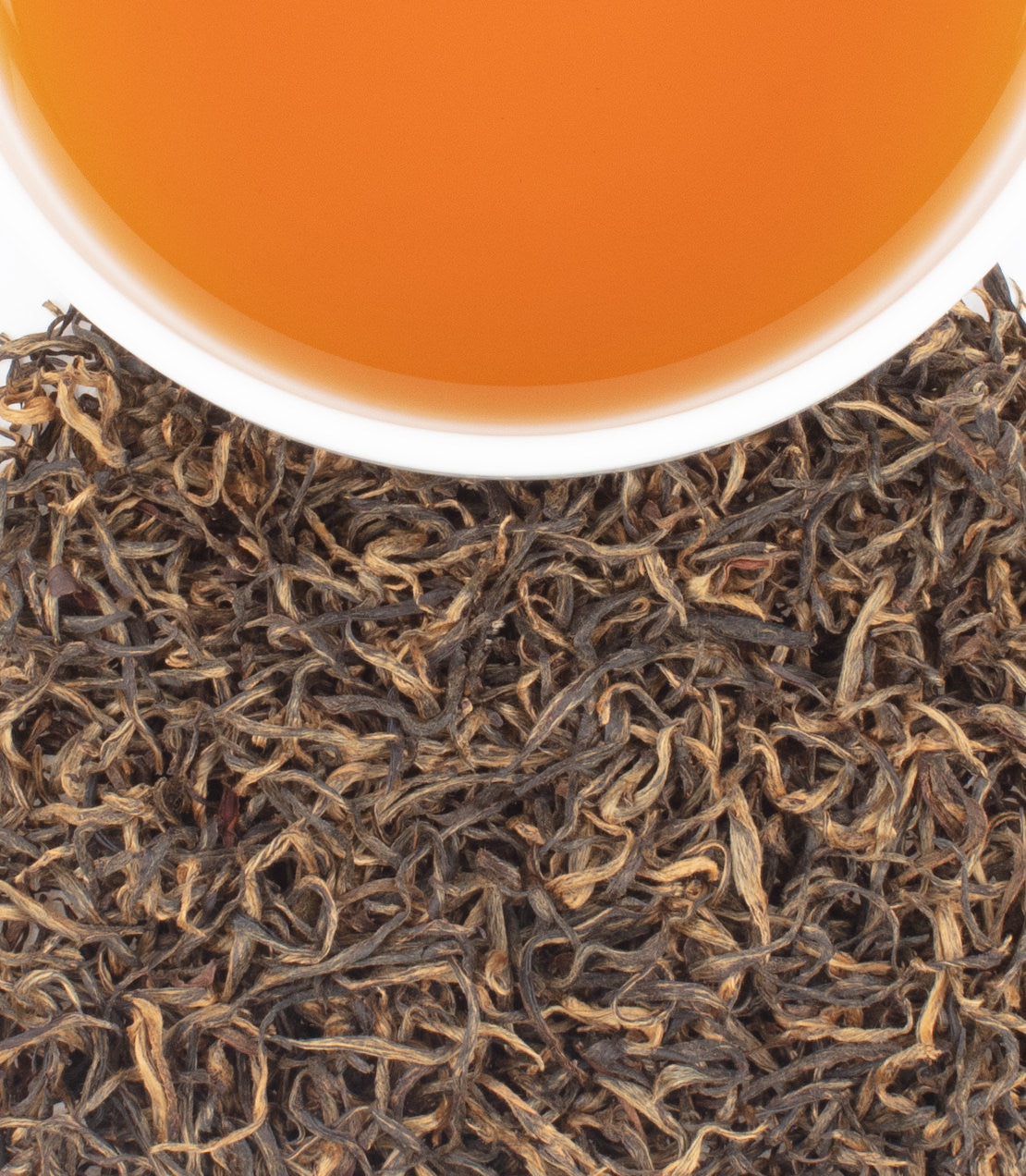 A cup of amber-colored tea sits above a pile of dark, twisted loose-leaf tea on a white background.