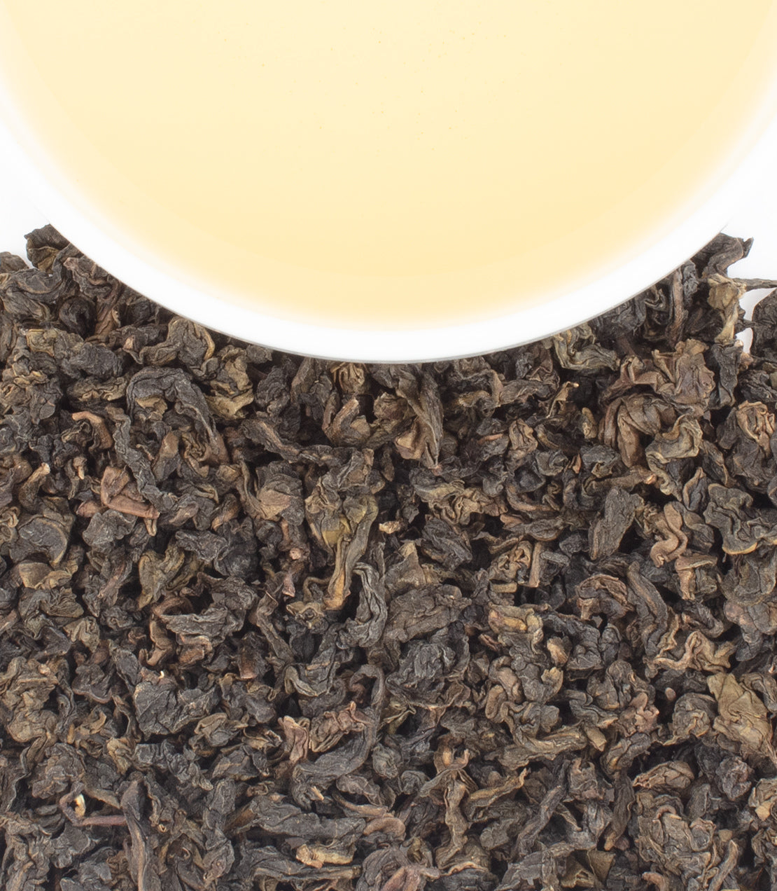 A cup of pale tea rests above a pile of dark, crinkled tea leaves.