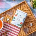 Tea packaging with tea bags on a woven tray next to a cup of tea.