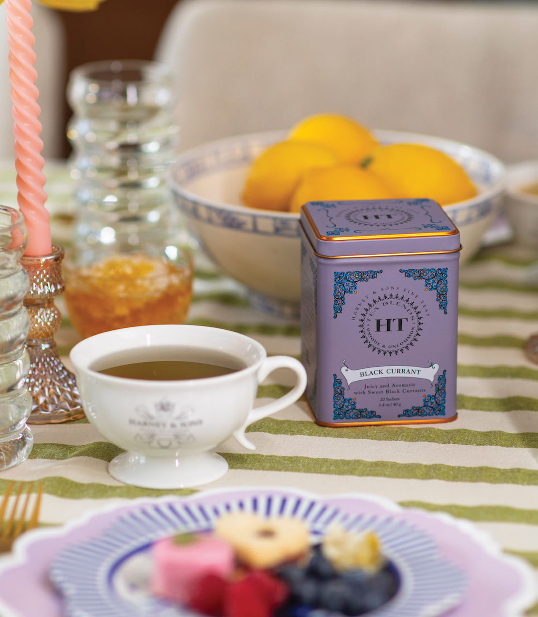 Black Currant HT tin of 20 sachets on a table with tea, fruits, and decorative tableware.