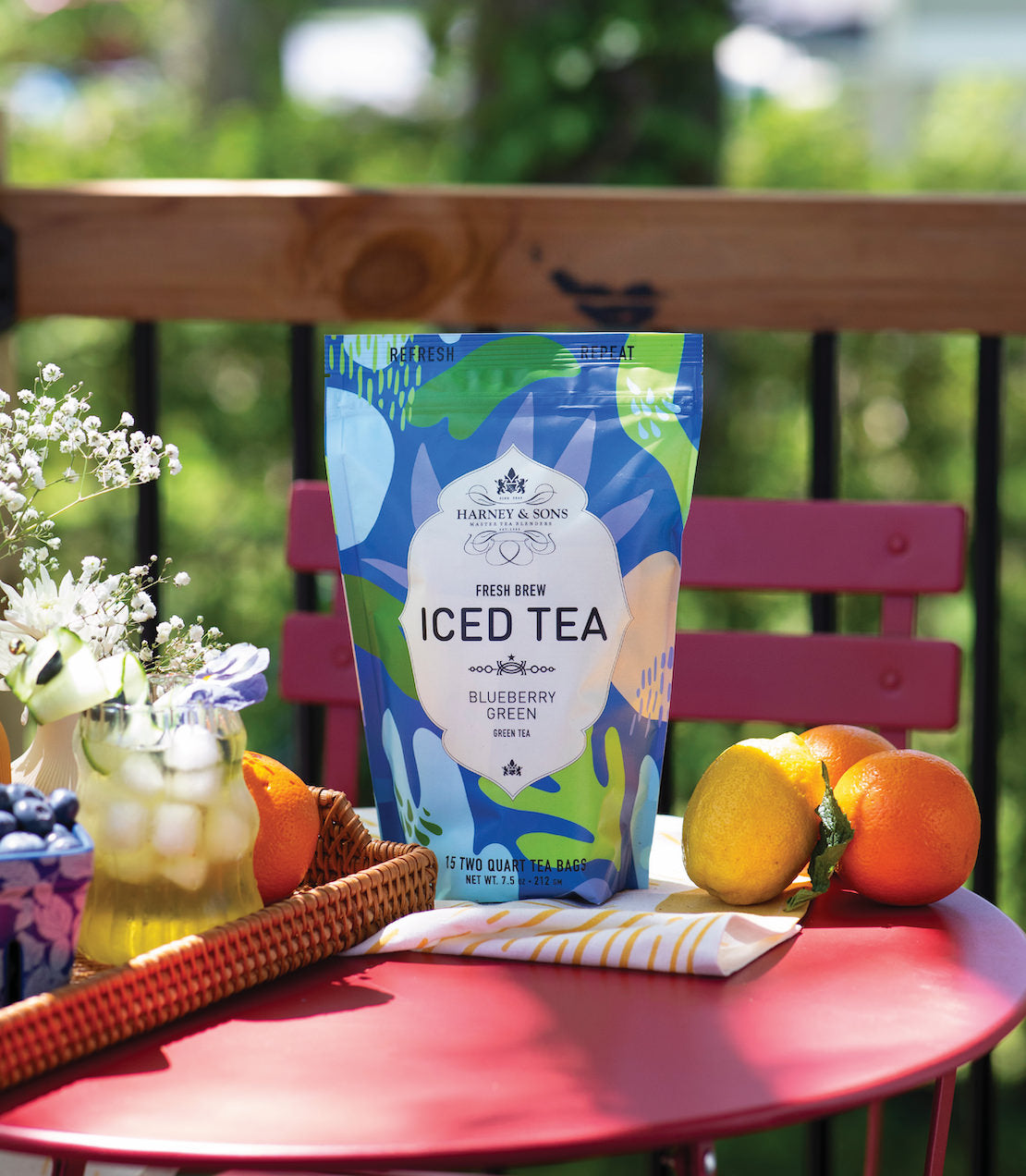 Brightly colored packaging of Blueberry Green Fresh Brew Iced Tea on a pink table, surrounded by fruits and flowers.