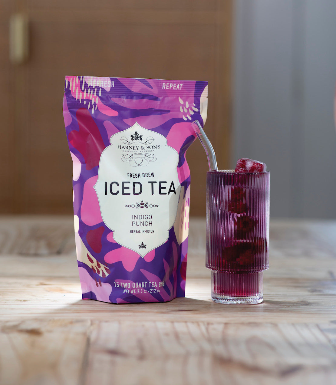 Indigo Punch Fresh Brew Iced Tea package beside a glass filled with iced tea and ice cubes on a wooden table.