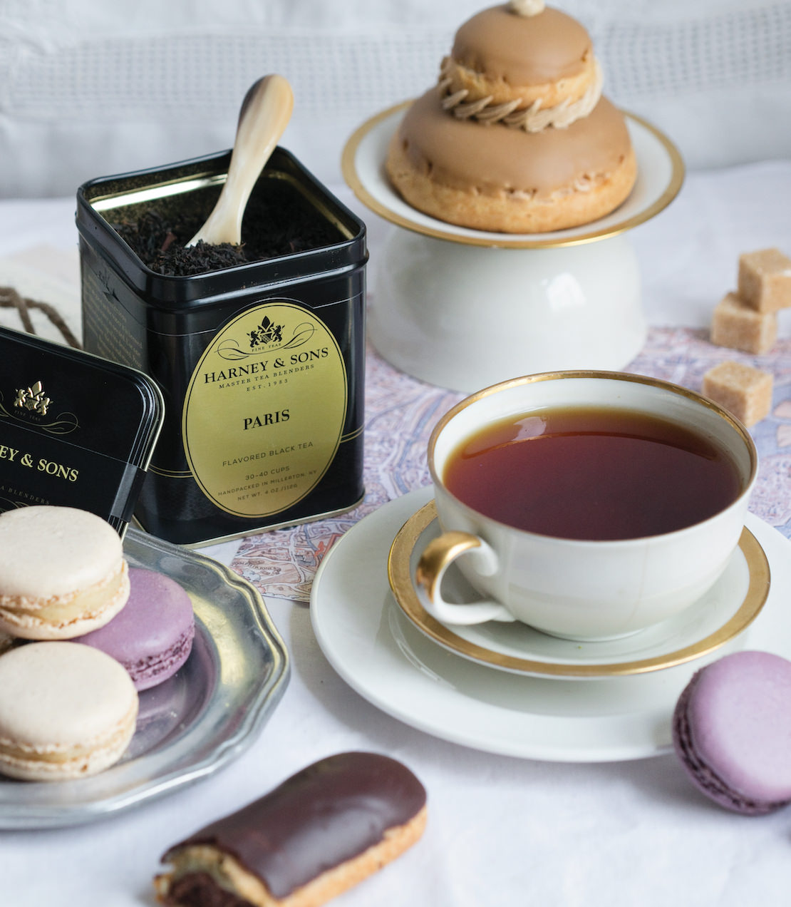 A cup of Paris-flavored black tea with macarons and pastries on a table, showcasing elegant tea time treats.