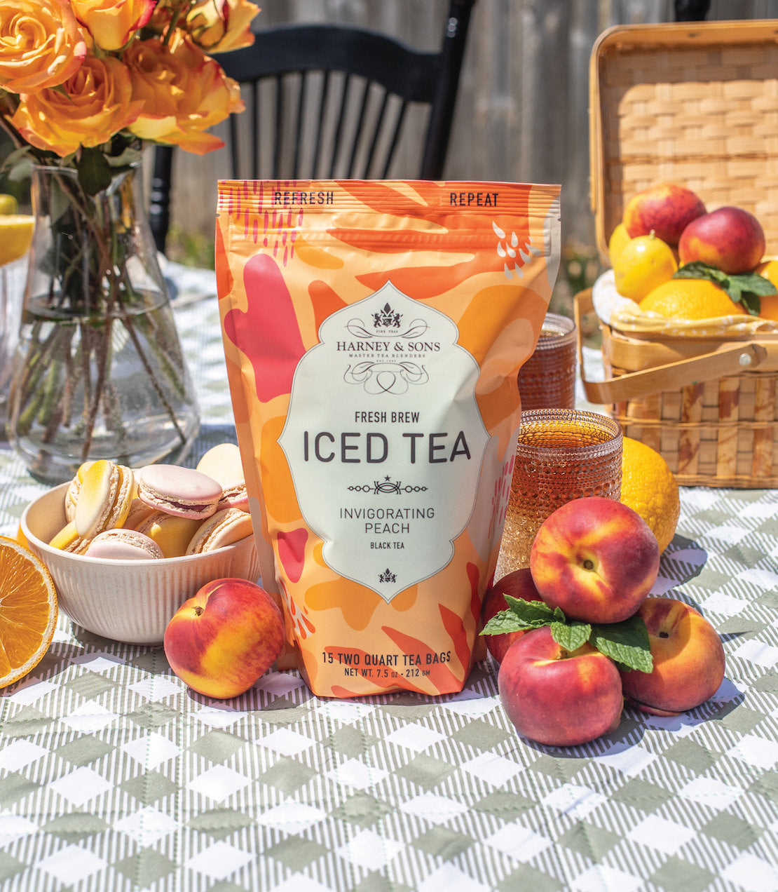 Harney & Sons Peach Fresh Brew Iced Tea bag with peaches and macarons on a picnic table, surrounded by flowers.