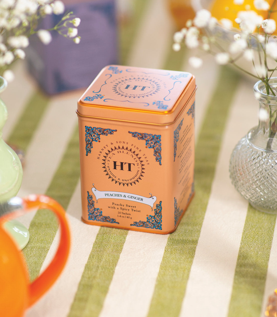 "Peaches & Ginger tea tin with 20 sachets, featuring a vibrant orange design and floral accents.