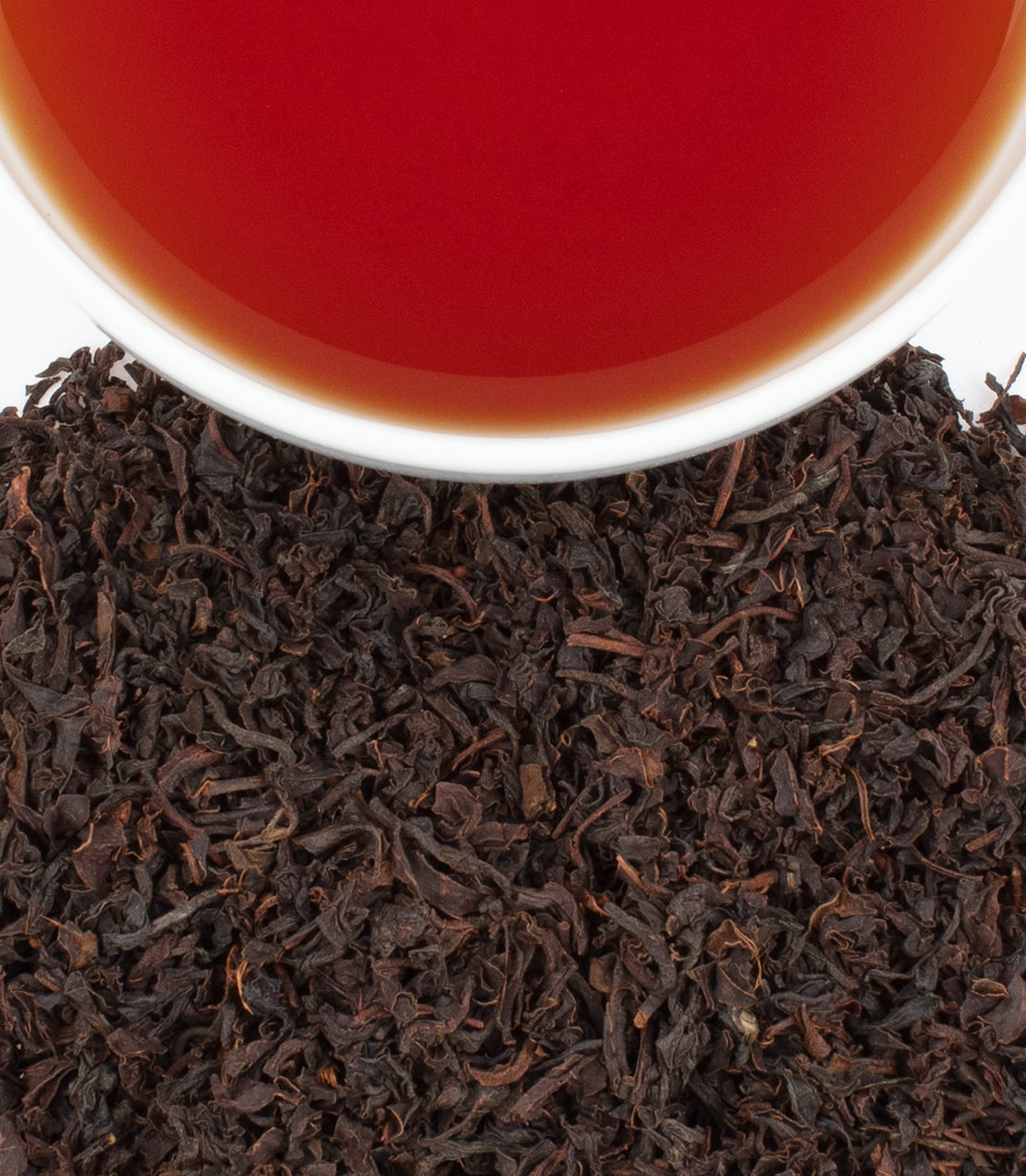 A close-up of organic Korakundah tea leaves with a cup of brewed tea above, showcasing rich color and texture.