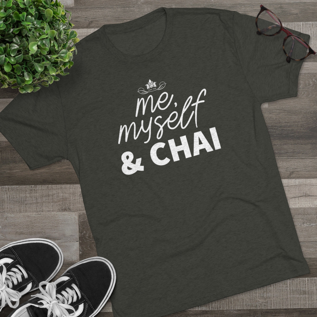 Olive green graphic tee featuring the text "me, myself & CHAI" in white, styled with casual sneakers and glasses.