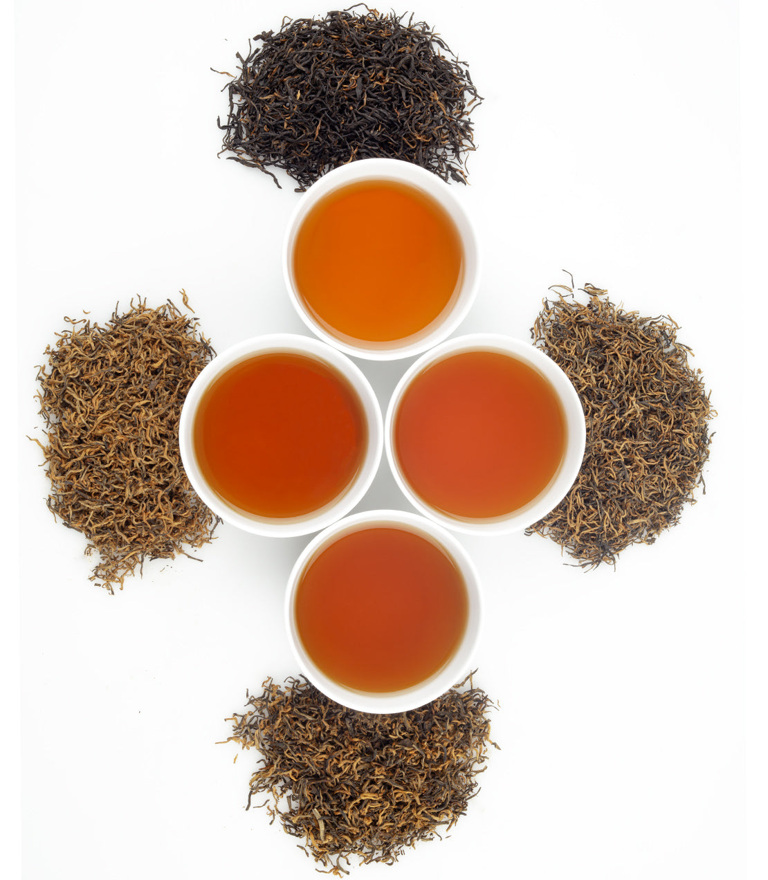 Four bowls of brewed tea surrounded by loose tea leaves, showcasing the rich colors and textures of Flight of the Golden Monkeys.