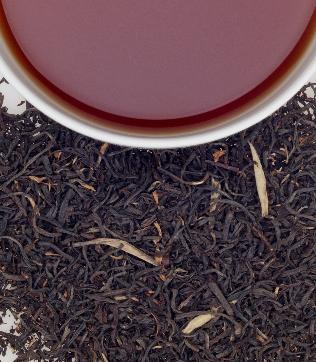 A cup of Anniversary Blend tea above loose black tea leaves, showcasing rich color and texture.
