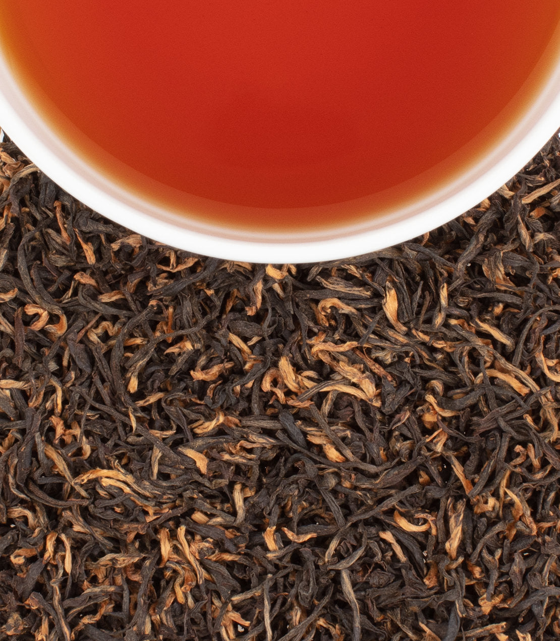 A close-up of Halmari Full Assam tea leaves with a cup of brewed tea, showcasing rich color and texture.