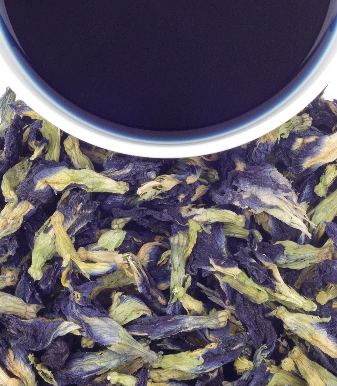 Dried butterfly pea flowers with a cup of brewed blue tea above, showcasing vibrant colors and natural ingredients.