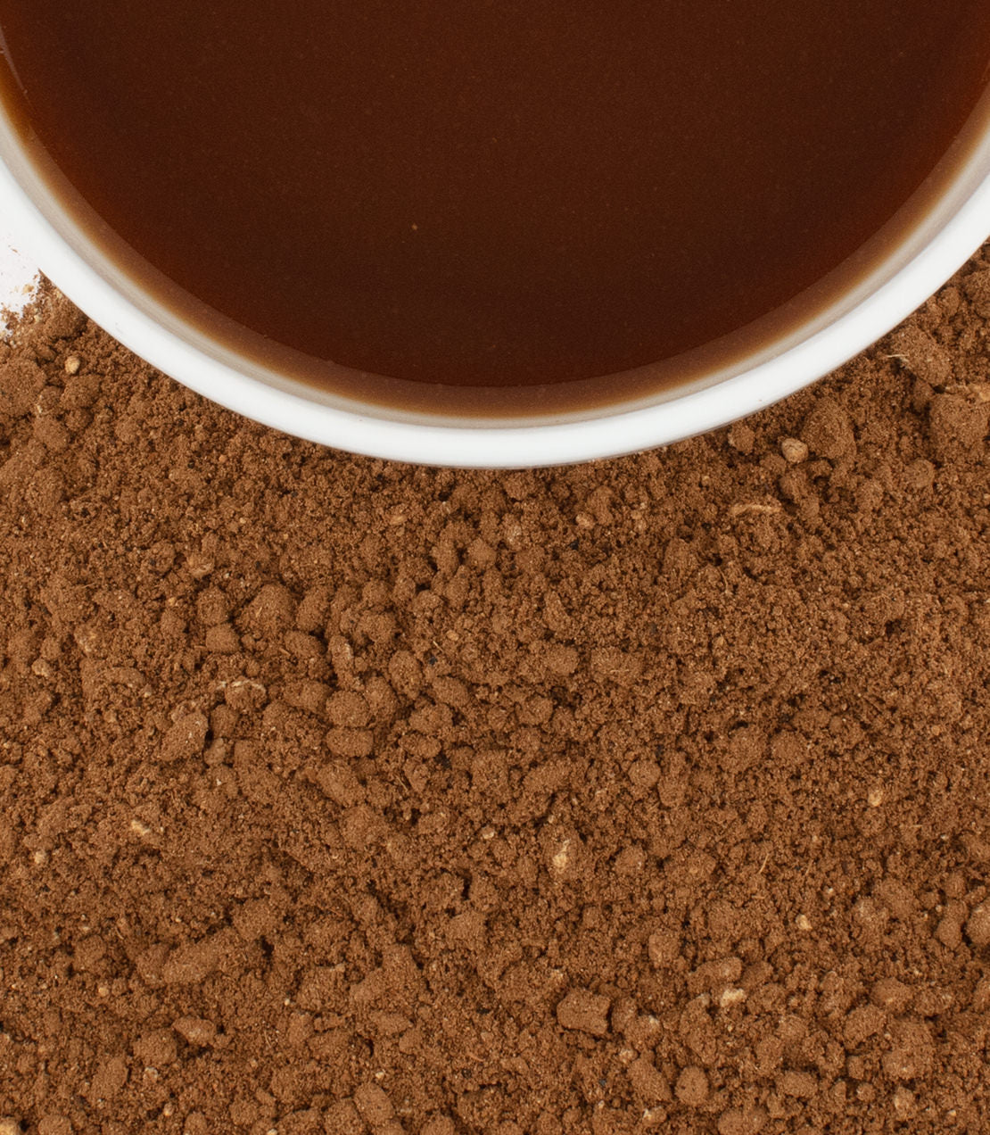 A cup of organic Chaga Chai tea surrounded by loose chai powder, highlighting a nourishing wellness blend.