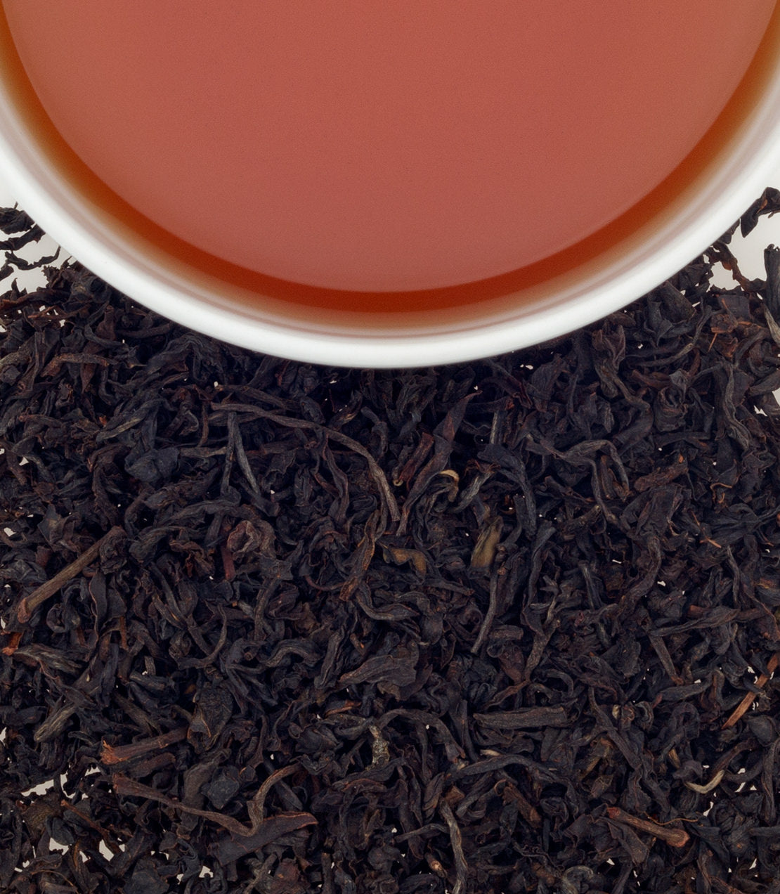 A cup of Chamraj Nilgiri FOP tea above loose black tea leaves, showcasing rich color and texture.