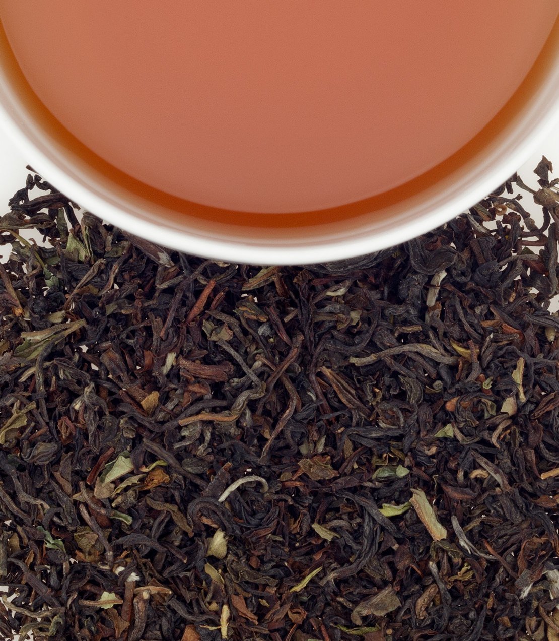 A cup of brewed Darjeeling tea above loose black tea leaves, showcasing its rich color and texture.