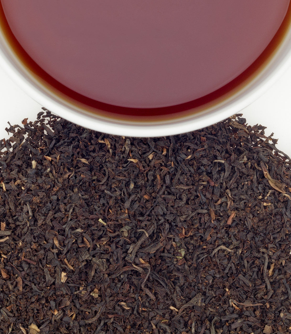 A cup of brewed East Frisian tea above a pile of loose black tea leaves, showcasing rich color and texture.