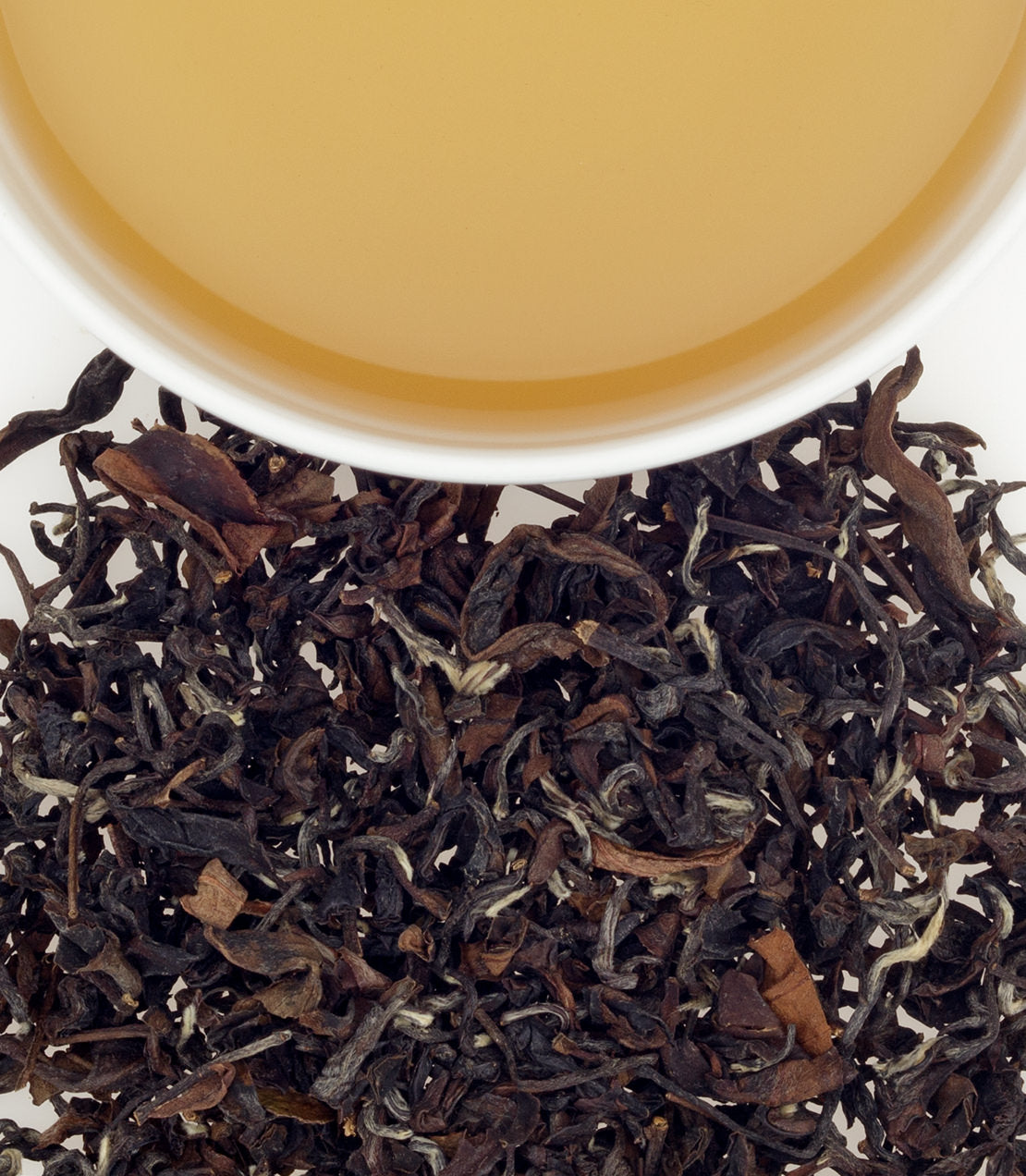Aerial view of Fanciest Formosa Oolong tea leaves and brewed tea in a white cup, showcasing rich colors and textures.