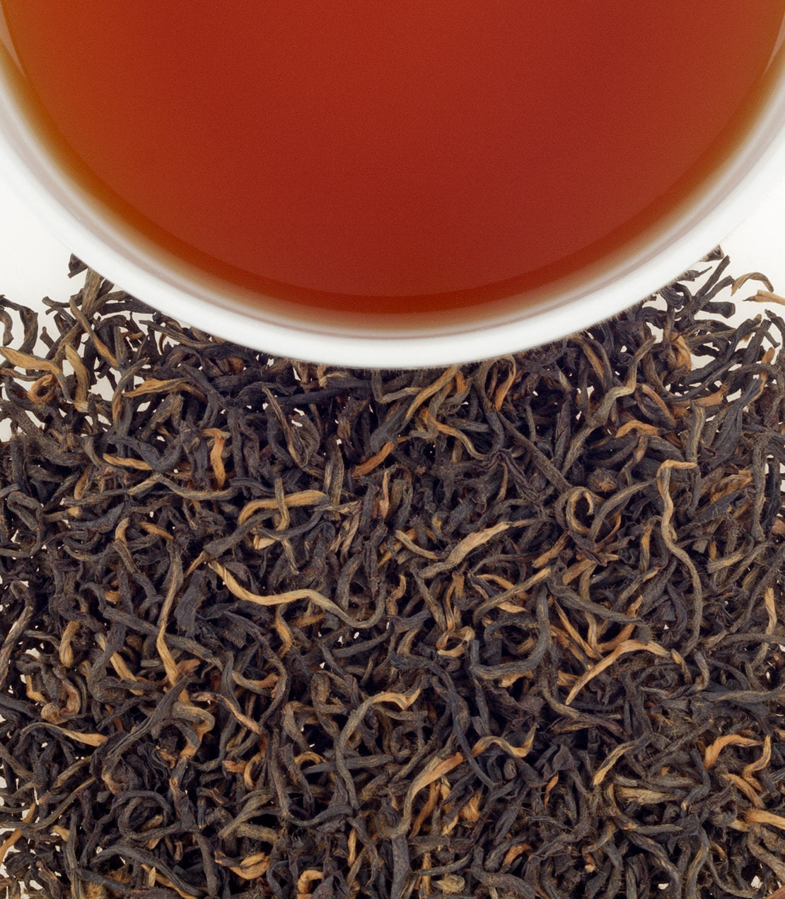 A close-up of loose black tea leaves with a cup of brewed golden tea above, showcasing rich color and texture.