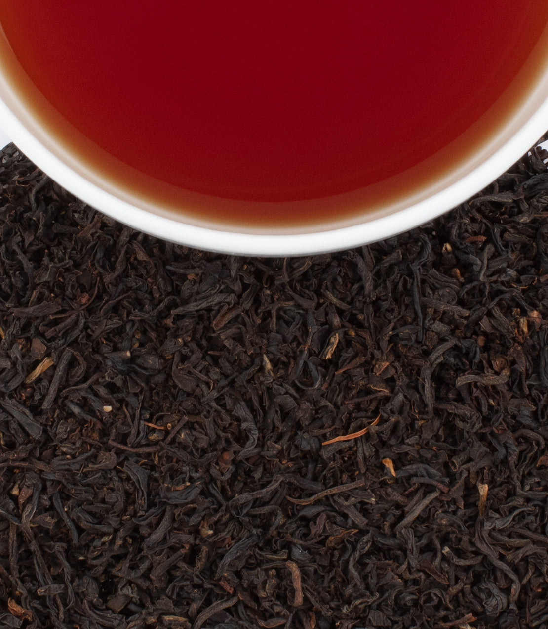 Royal English Breakfast tea in a white cup above loose black tea leaves, showcasing rich color and aroma.