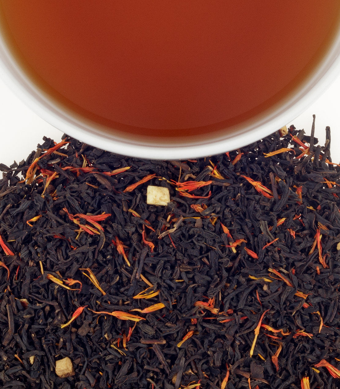 A close-up of loose holiday tea leaves with vibrant saffron strands, next to a steaming cup of brewed tea.
