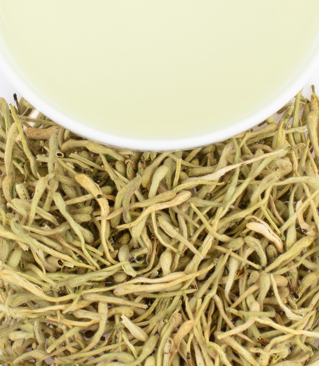 Dried honeysuckle flowers with a cup of light green tea above, showcasing natural herbal ingredients.