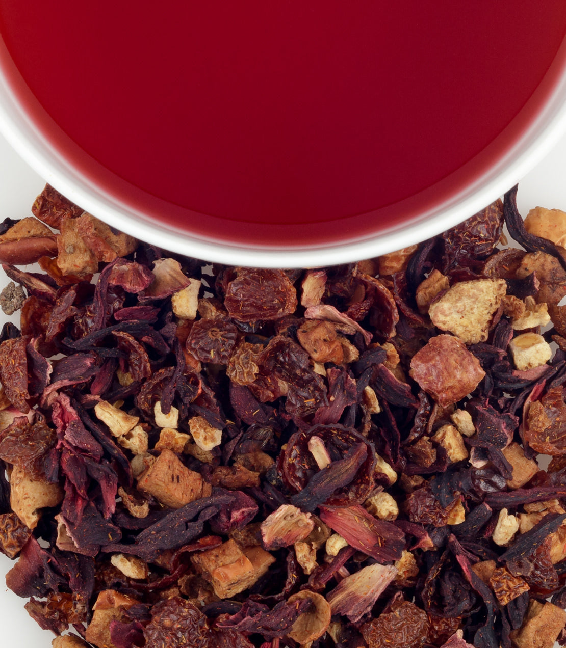 A cup of vibrant orange passion fruit tea above a blend of dried fruit and herbs.