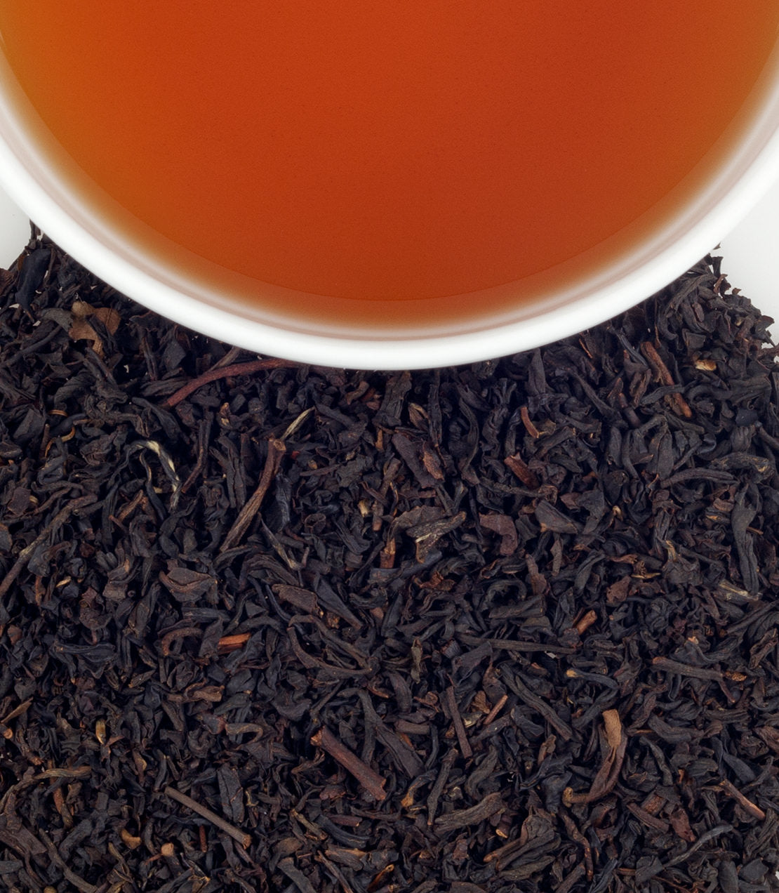 A close-up of a cup of brewed tea above a pile of loose black tea leaves, showcasing rich colors and textures.