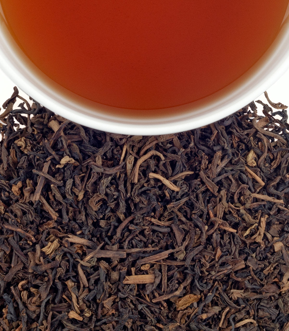 A cup of brewed Decaf Vanilla Comoro tea above loose black tea leaves, showcasing rich color and texture.