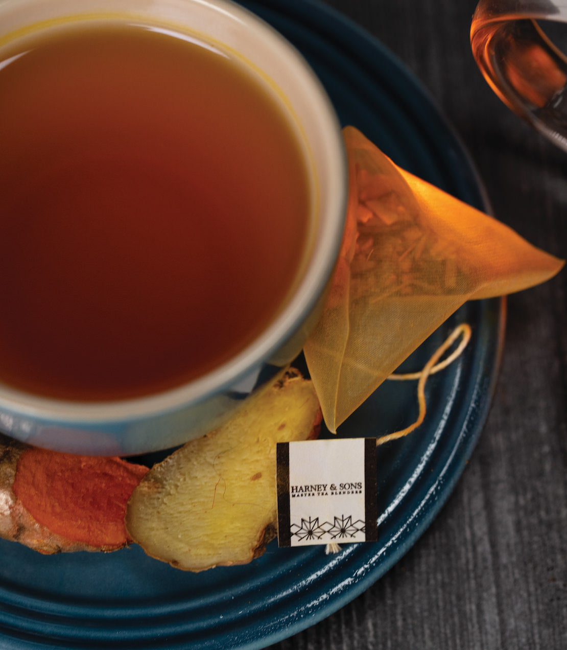 Organic Ginger Turmeric tea in a cup, with a sachet and dried ginger pieces on a blue plate.