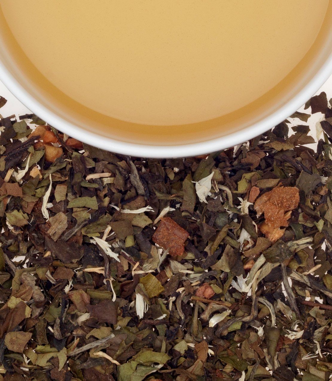 A close-up of dried tea leaves with a cup of light-colored tea above, showcasing herbal ingredients.