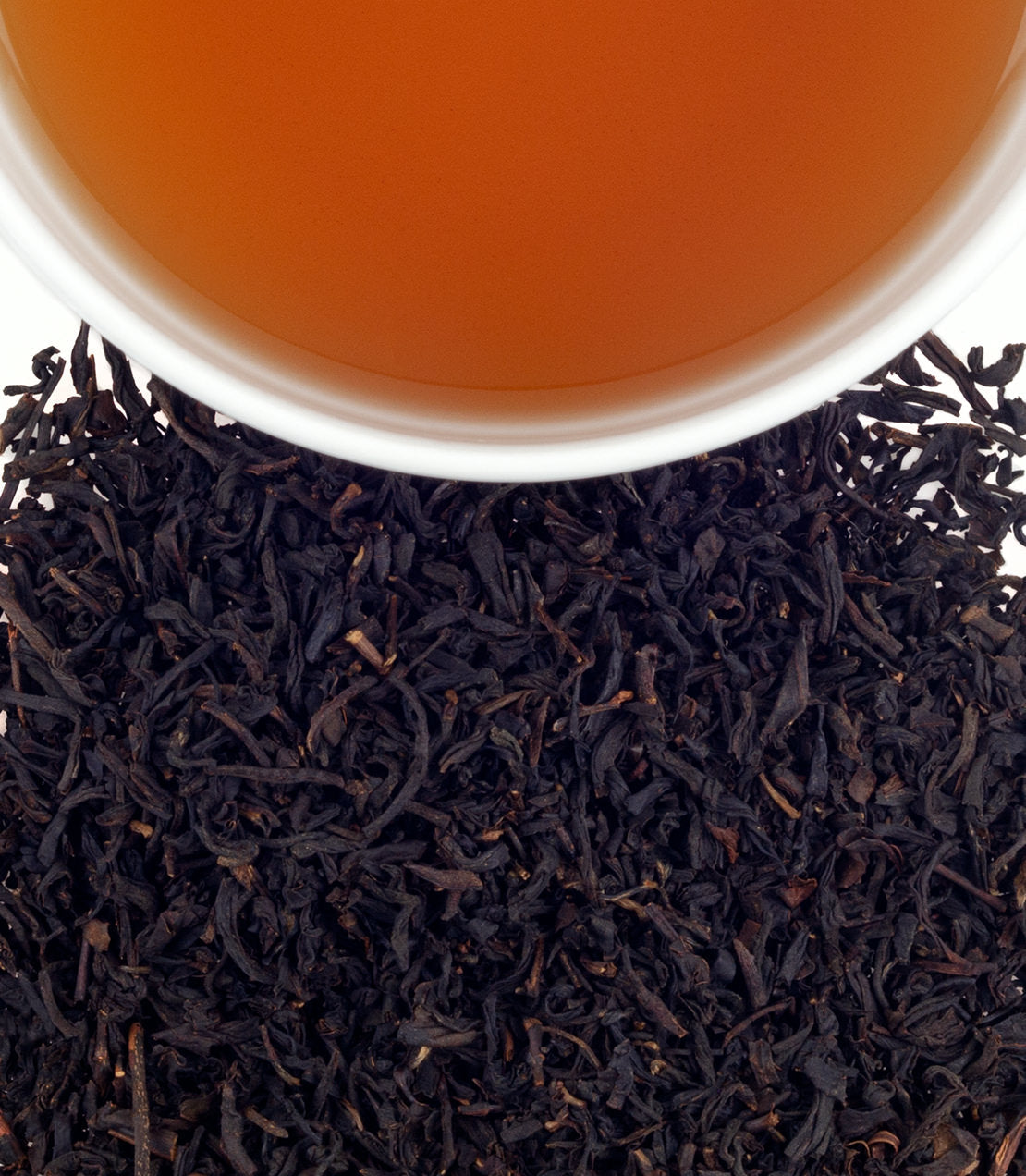 A close-up of loose black tea leaves with a cup of brewed vanilla black tea above.