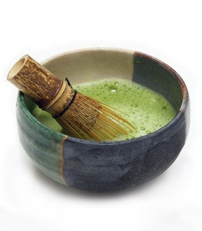 Bowl of matcha tea with a bamboo whisk, showcasing vibrant green color and smooth texture.
